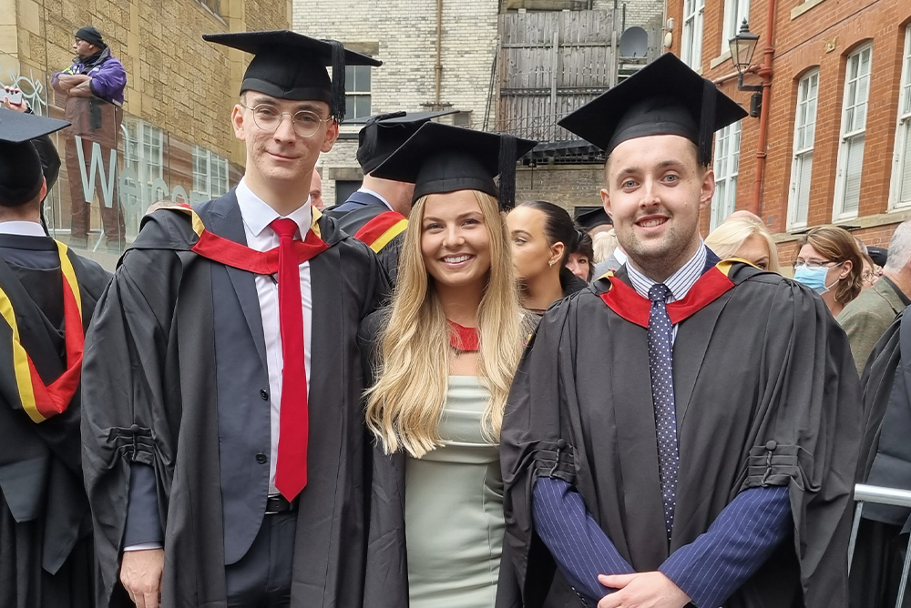 Three students pose in graduation gowns and hats